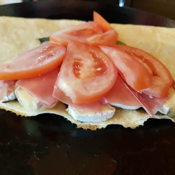 Savory Crepery crepe with sliced tomatoes, ham, and cheese on a griddle.