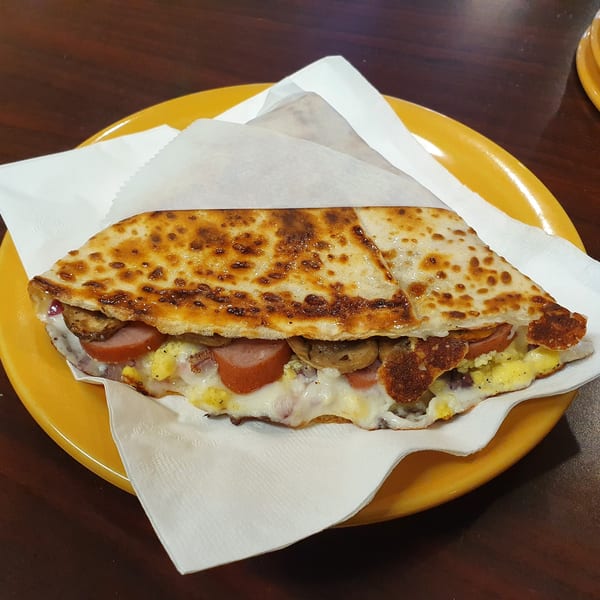 Savory Crepery crepe filled with sausage, scrambled eggs, mushrooms, and melted cheese on a yellow plate.