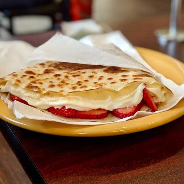 A golden-brown crepe from The Crepery, filled with fresh strawberries and white cream, on a yellow plate.