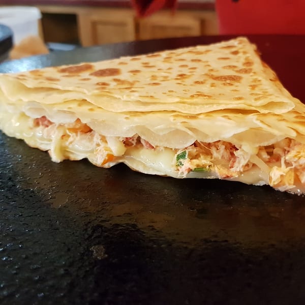 A savory crepe from The Crepery, filled with melted cheese and shredded chicken, on a griddle.